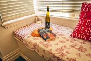 glencoe country b&b comfy window seat with bottle of wine, half a glass of wine and a novel